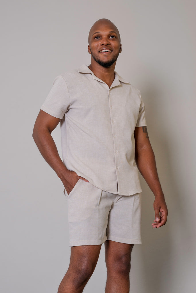 Men’s Cuban Short Sleeve Shirt in Beige, featuring a button-up front, Cuban collar, short sleeves, and a tapered fit. Model wearing shirt in a relaxed, casual setting