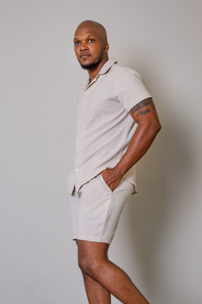 Men’s Cuban Short Sleeve Shirt in Beige, featuring a button-up front, Cuban collar, short sleeves, and a tapered fit. Model wearing shirt in a relaxed, casual setting