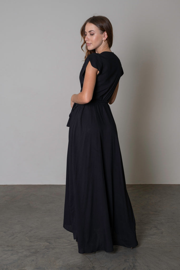 Maxi length wrap dress in black with a waist tie and flattering silhouette. Showing the back view.